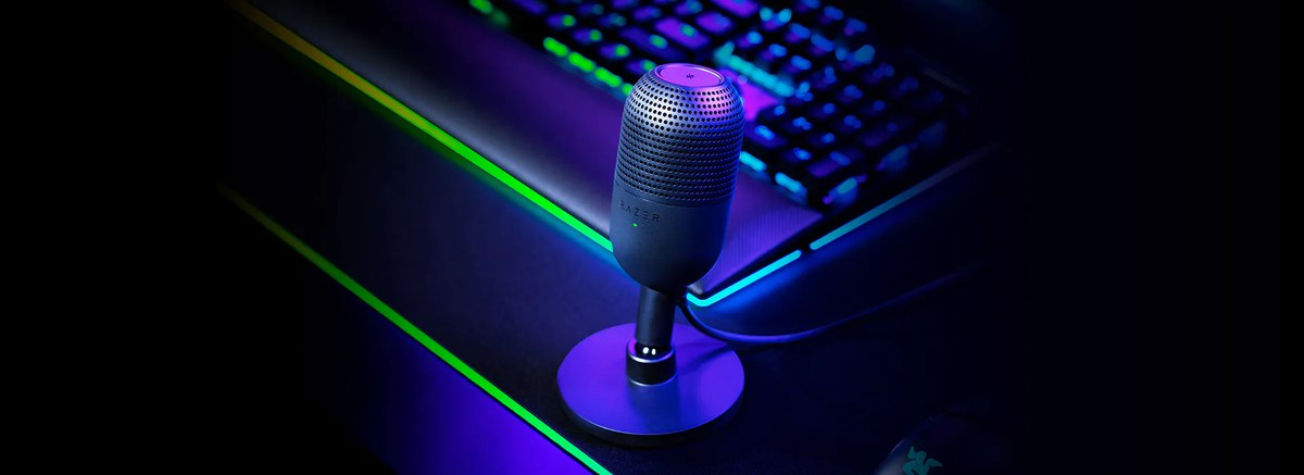 Razer Seiren V3 Mini USB 麥克風官方宣傳圖，機身極小立於桌面鍵盤旁，頂部為輕觸靜音感應區